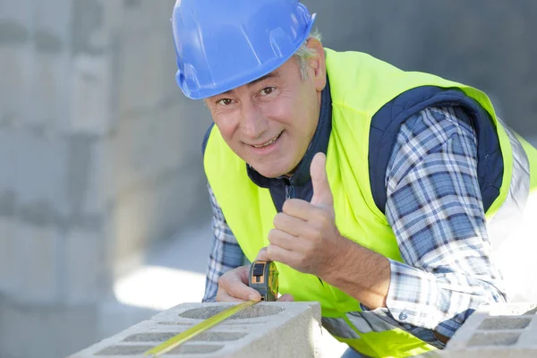 Senior Builder Measuring Concrete Block Holding Thumbs — Stock Photo, Image