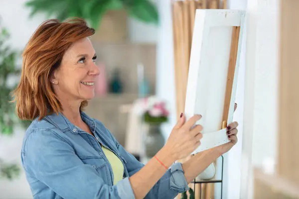mature woman hanging picture on wall