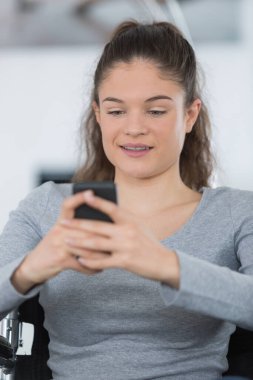 young woman on the wheelchair using a smartphone clipart