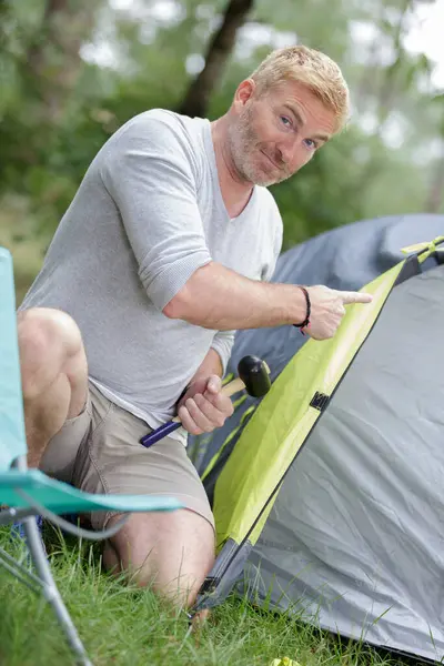 man with hammer pitching tent