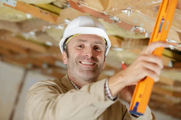 Manlig Byggnadsarbetare Som Använder Nivå För Att Mäta Takets Kvalitet Stockfoto