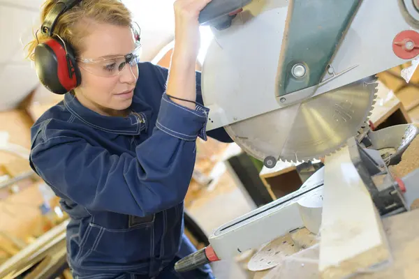 woman with safety goggles ear protection next to circular saw
