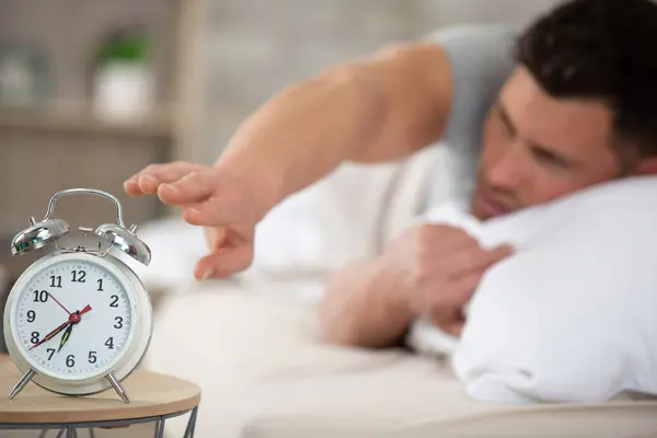 sleepy man in bed reaching for his alarm clock