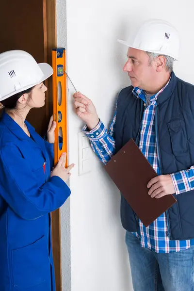 Female Apprentice Checking Level Door Frame While Architect Supervises Imagem De Stock