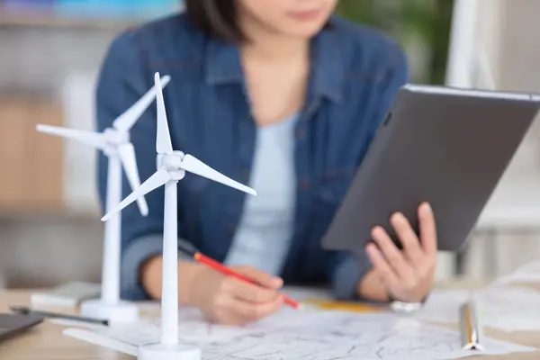 女人拿着模型风力涡轮机坐在办公桌前 免版税图库照片