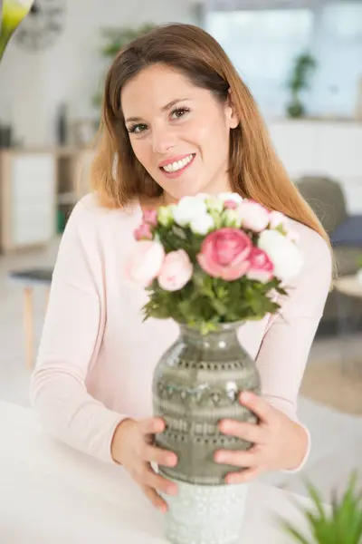 在家里拿着玫瑰花瓶的女人 免版税图库照片