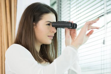 young woman searching with binoculars through blinds clipart