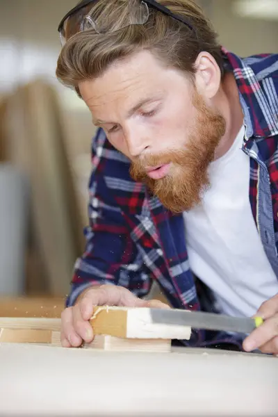 stock image man blows sawdust off the wood after sanding