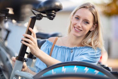 young woman adjusting seat on bicycle clipart