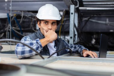 contemplative workman using laptop in roofspace clipart