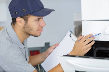 young serviceman with clipboard looking at oven clipart