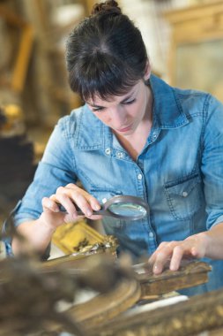 woman using a magnifying glass to inspect a frame embellishment clipart