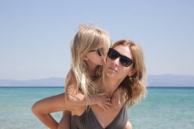 Anne, kızını sahilde sırtında taşıyor. Mutlu huzurlu aile yaz tatili konsepti.