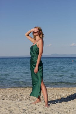 Gecelik zümrüt yeşili ipek saten uzun elbise içinde güzel genç manken, sahilde moda yaz portresi.