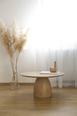 Oturma odasının içi sıcak bej tonlarda, sehpa sehpası katı ahşaptan ve kurutulmuş otlardan yapılmış vazodan yapılmış doğal güneş ışığı dallarıyla dolu.. 