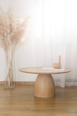 Oturma odasının içi sıcak bej tonlarda, sehpa sehpası katı ahşaptan ve kurutulmuş otlardan yapılmış vazodan yapılmış doğal güneş ışığı dallarıyla dolu.. 