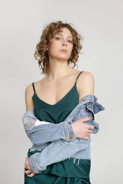 クラシックなブルーデニムジャケットをレイヤードシルクドレスを身に着けている女性モデル スタジオで撃たれた 季節の移行のためのカジュアルかつスタイリッシュな衣装 — ストック写真