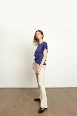 Stüdyo fotoğrafları, basit rahat kıyafetler, mavi bluz, beyaz pantolon ve mokasen ayakkabı giyen genç kadın modeller.