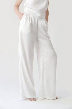 Beyaz ipek elbiseli, kolsuz bluzlu ve geniş bacaklı genç bir modelin seri fotoğrafları.