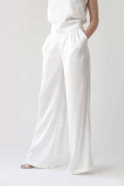 Beyaz ipek elbiseli, kolsuz bluzlu ve geniş bacaklı genç bir modelin seri fotoğrafları.