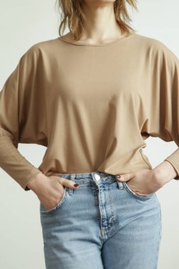 Studio photo of young female model wearing blue jeans and beige shirt made from organic cotton.