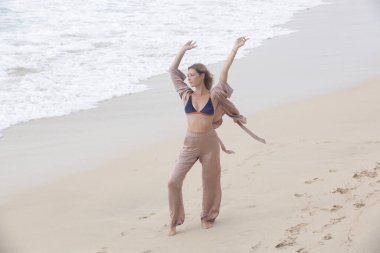 Beautiful serene woman with raised arms on the sand beach enjoying nature, freedom and fresh sae air, concept of happiness, mindfulness and being present in the moment.