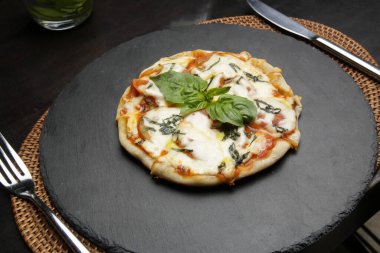 Pizza Margherita with with tomatoes, basil and mozzarella cheese on black stone tray.  