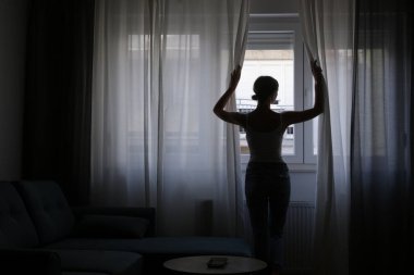 Dairenin perdelerini açan kadın silueti.