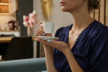 Rahatlamış genç bir kadın oturma odasında bir fincan kahvenin tadını çıkarıyor, ev konseptinde kendi kendine bakım gününü rahatlatıyor.