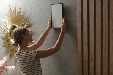 Yeni evin duvarlarında resim çerçeveleri düzenleyen kadın, ev geliştirme konseptini bozuyor.