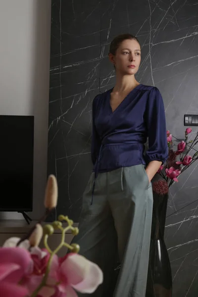 Woman in dark blue satin blouse in the apartment, elegant and comfortable look.