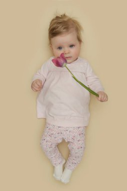 Adorable five months old baby with pink spring tulips. Herald of spring. Baby and infant milestone session. Spring composition. Photoshoot of newborns. March 8 or Easter postcard concept.