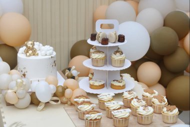 Creative gender neutral baby shower or birthday decoration in the garden. Bohemian style outdoor event set up with balloons. White cream peach caramel balloon arch kit. Sweet table for a party