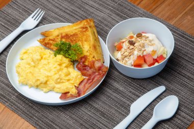 Çocuk menüsü, çırpılmış yumurta, pastırma, tost ve yoğurtlu müsli restoran masasında servis edilen plastik çocuklarla birlikte..
