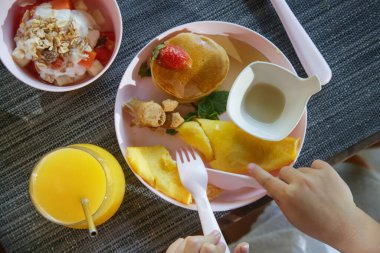 Çocuk menüsü - omlet, akçaağaç şuruplu krep, yoğurtlu müsli ve restorandaki masada servis edilen taze meyve suyu ve plastik çocukların yediği çatal bıçak..