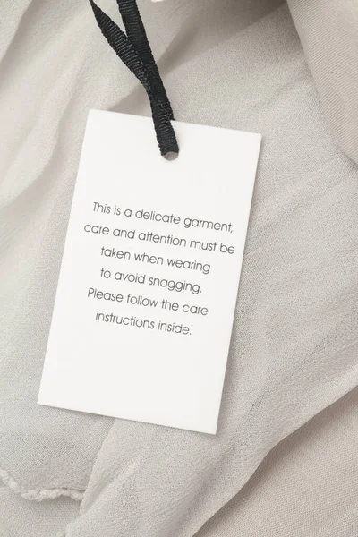 Close up of luxury clothing hang tag. Delicate garment swing tag. Laundry care washing instructions clothes label.