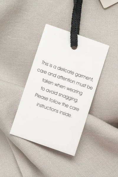 Close up of luxury clothing hang tag. Delicate garment swing tag. Laundry care washing instructions clothes label.