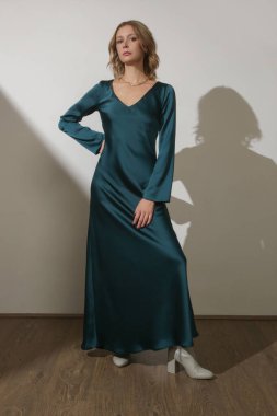 Stüdyo fotoğrafları. Uzun kollu, maksimum yeşil ipek elbise giyen genç bir kadın model.