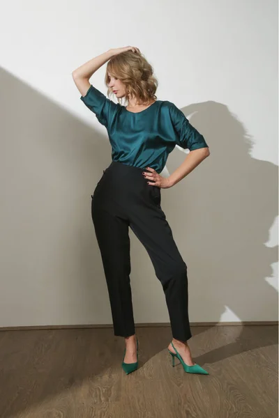 穿着绿色绸缎衬衫和黑色高耸长裤的年轻女模特的摄影棚照片系列 — 图库照片