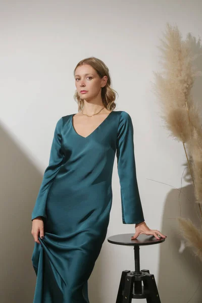 Serie of studio photos of young female model wearing maxi green silk dress with long sleeves