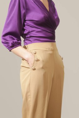 Stüdyo fotoğrafları, menekşe ipek saten bluz ve bej renkli yüksek paçalı pantolon giyen genç bir kadın model.