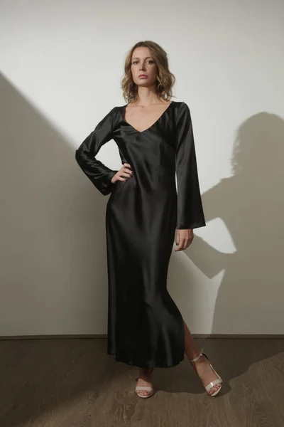 Serie of studio photos of young female model wearing maxi black silk dress with long sleeves