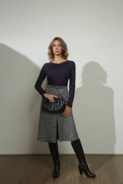 Yapışkan gömlek ve desenli yünlü etek giyen genç bir modelin stüdyo fotoğrafları.