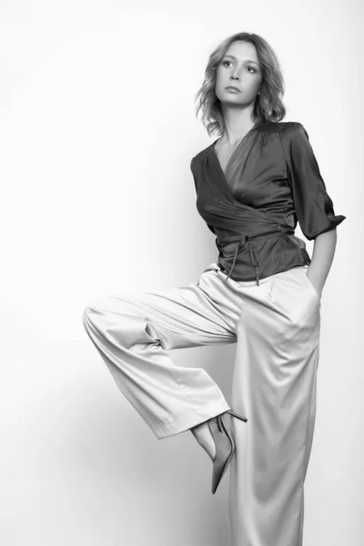 シルクサテンラップブラウスとワイド足のズボンを身に着けている若い女性モデルの黒と白のファッションの肖像画 — ストック写真
