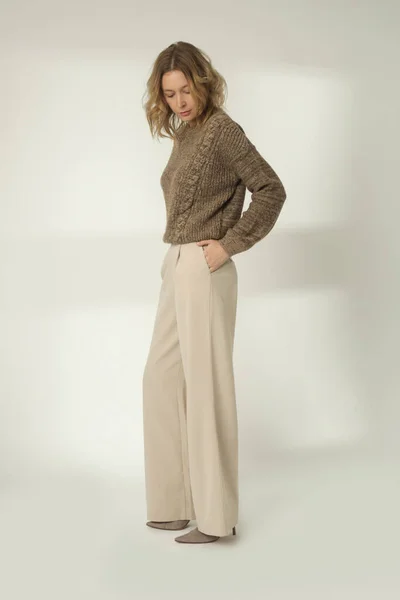 茶色の冬のセーターと白の背景にベージュワイドパンツの若い女性のファッション肖像画 — ストック写真