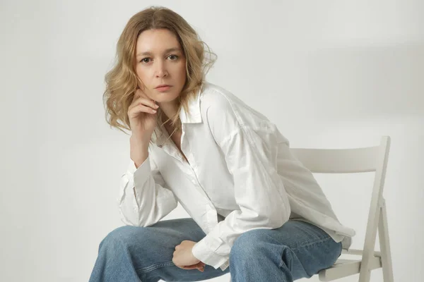 白色背景下穿着白色棉纽扣衬衫和蓝色牛仔裤的年轻女子的时尚肖像 — 图库照片