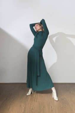 Stüdyo fotoğrafları. Uzun kollu, maksimum yeşil pamuklu bir elbise giyen genç bir kadın model.