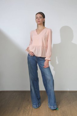 Stüdyoda çekilen zarif bluz ve rahat kot pantolonlu genç kadın fotoğraflarının serisi.