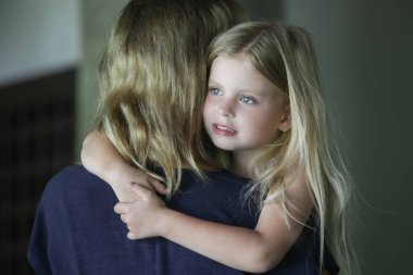 Sevimli küçük kız annesine sarılıyor ve kameraya bakıyor.