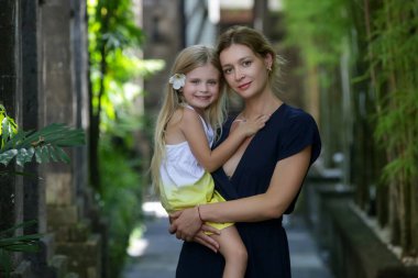 Anne ve kızı tropik otelin arka sokağında poz veriyorlar, aile yaz tatili konsepti, hatıralar yaratıyorlar.